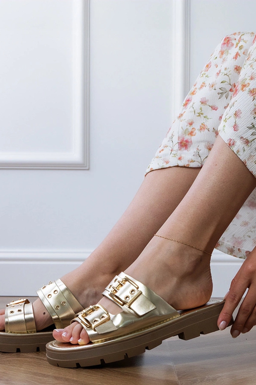 Gouden platte slippers met gespen op...